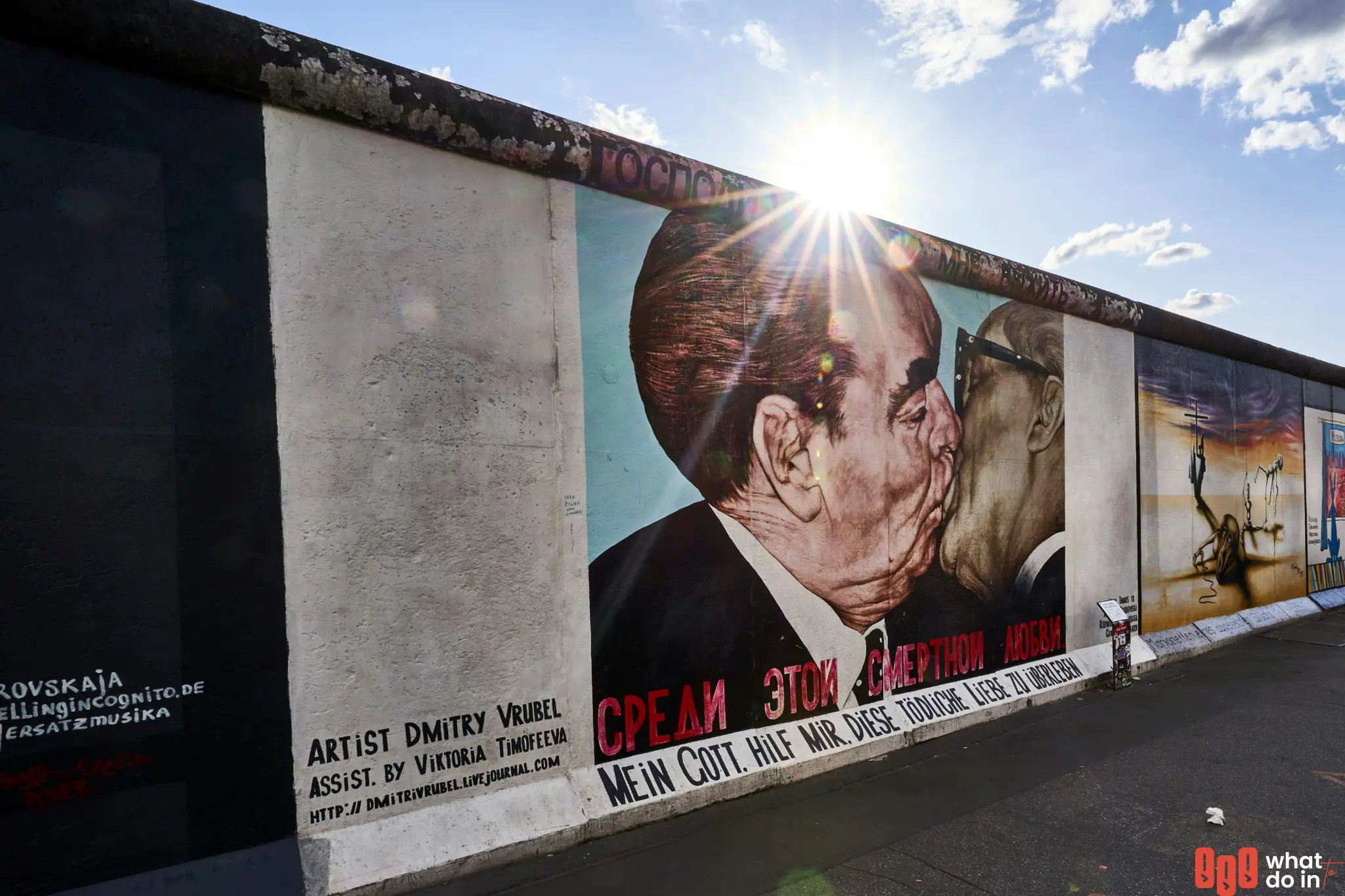 Famous mural 'My God, Help Me to Survive This Deadly Love' by Dmitri Vrubel at the Berlin East Side Gallery, depicting a socialist fraternal kiss between Leonid Brezhnev and Erich Honecker, painted on a preserved section of the Berlin Wall under bright sunlight.